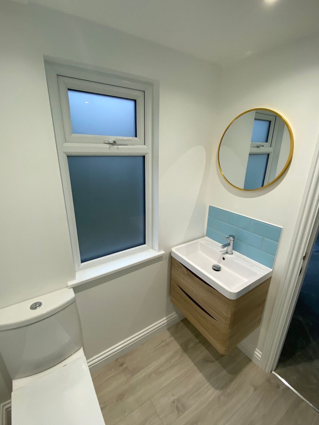 Newly fitted bathroom, white walls, small window and a mirror above the sink